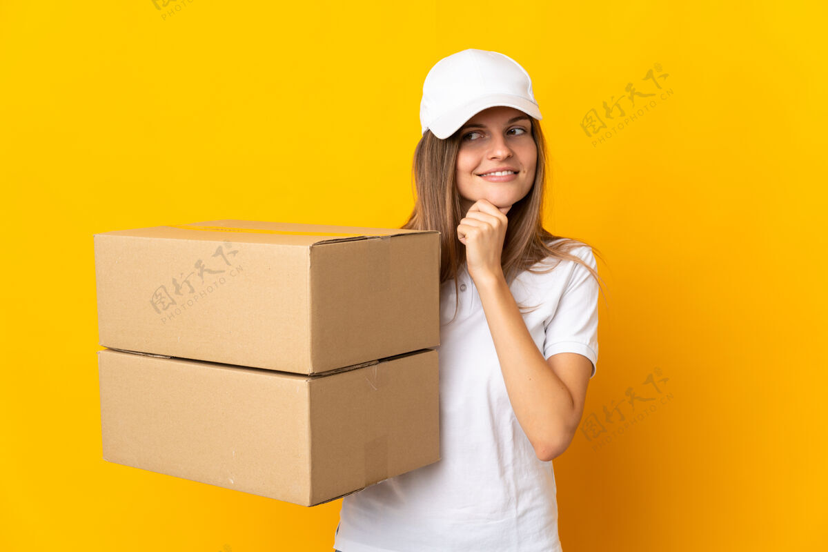 邮政年轻的斯洛伐克女送货员孤立在黄色的墙上 面带微笑地看着旁边快递大笑肖像