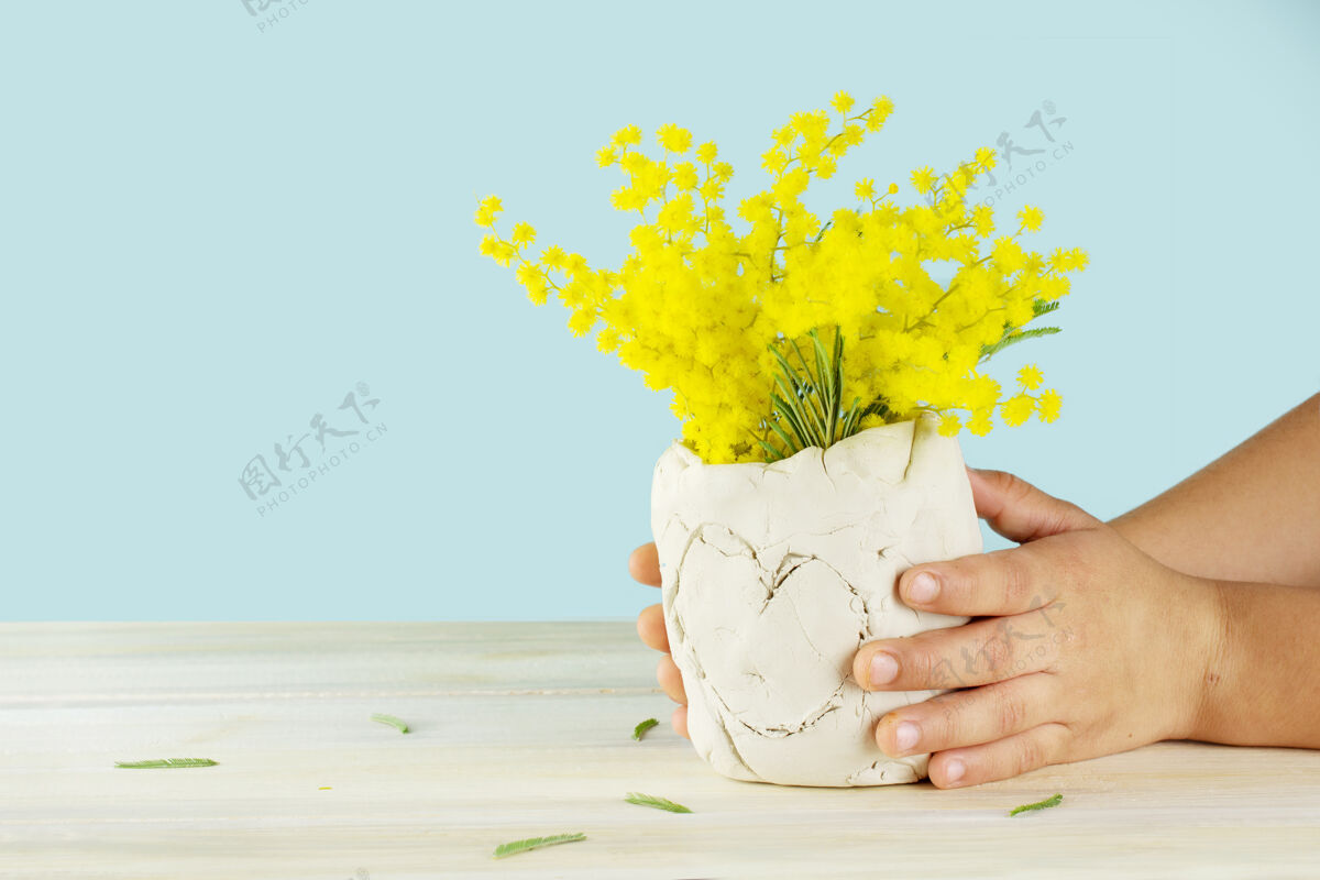 花束孩子的手拿着一个黄色花朵的diy陶瓷花瓶孤立在蓝色的表面上自然孩子复制空间