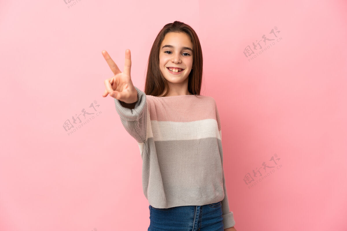 是的被隔离在粉红色墙上的小女孩微笑着 展示着胜利的标志手势胜利模型