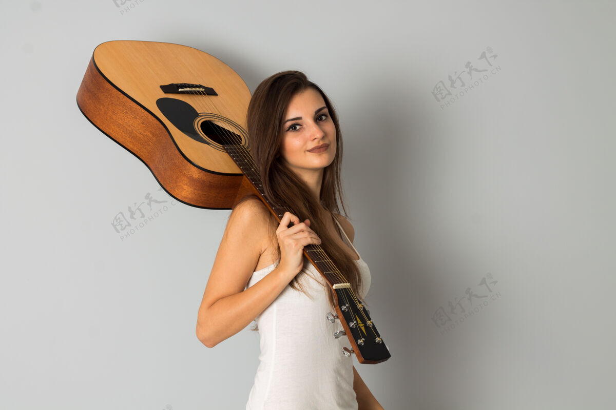 歌曲在灰色墙上的摄影棚里 一个黑发女人手里拿着吉他看着摄像机的画像声学音乐女人