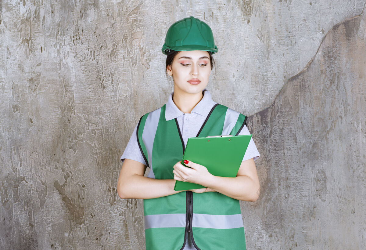 晋升身着绿色制服 头戴安全帽的女工程师拿着项目文件夹建筑师工人报告