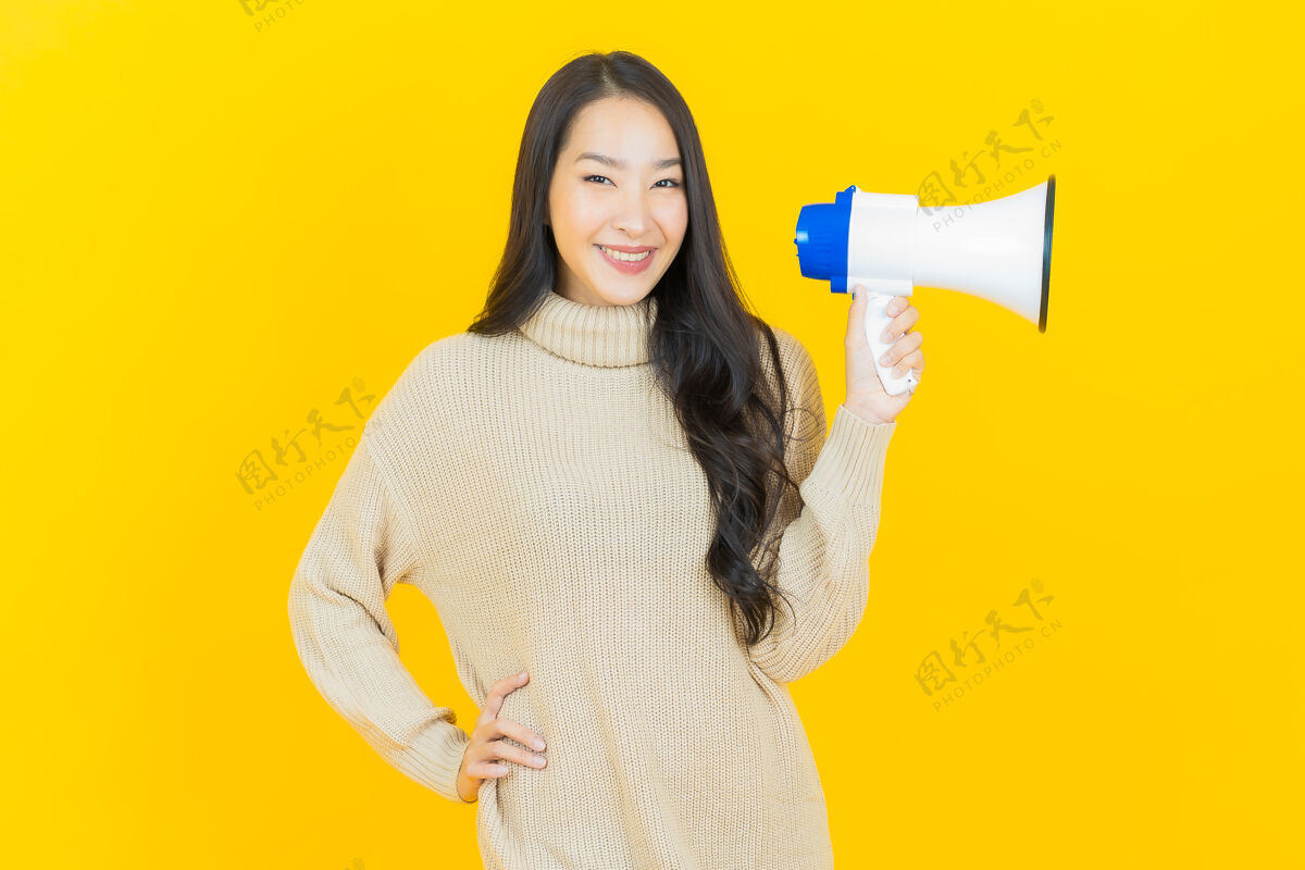 沟通美丽的亚洲年轻女子在黄色墙上用扩音器微笑快乐说话抱着