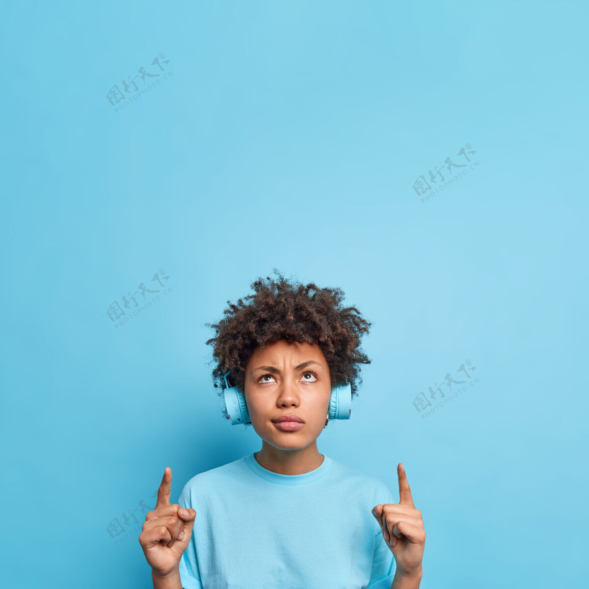 指向严重不满的非裔美国女孩卷发点食指以上显示广告反对蓝墙听音乐通过无线耳机对产品价格高不满外观情绪黑发