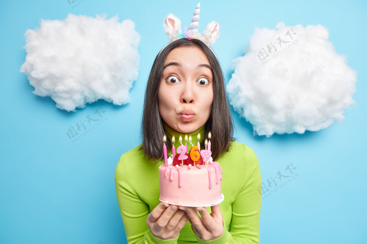满意女人屏住呼吸吹蜡烛在生日蛋糕上许愿庆祝26日穿绿色高领毛衣和独角兽头带举行甜点欢乐
