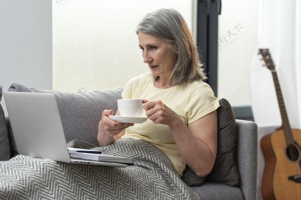 老年人家里的老太太在沙发上用笔记本电脑喝咖啡养老金老年人内部