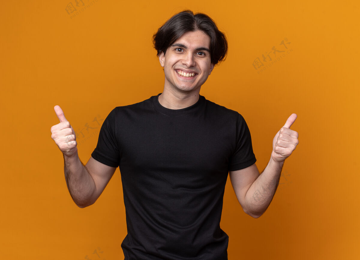 姿势笑容可掬的年轻帅哥 穿着黑色t恤 竖起大拇指 孤零零地站在橙色的墙上衣服感觉市民
