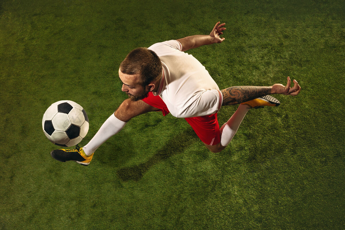 动作白种人足球或足球运动员在草地上的绿色背景俯视图年轻男性运动模型训练 练习 踢球 进攻 接球运动概念 比赛 胜利单人球员青少年