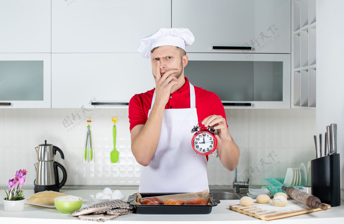 房子顶视图年轻的男厨师拿着时钟 在白色的厨房里感到困惑男厨师烹饪顶部