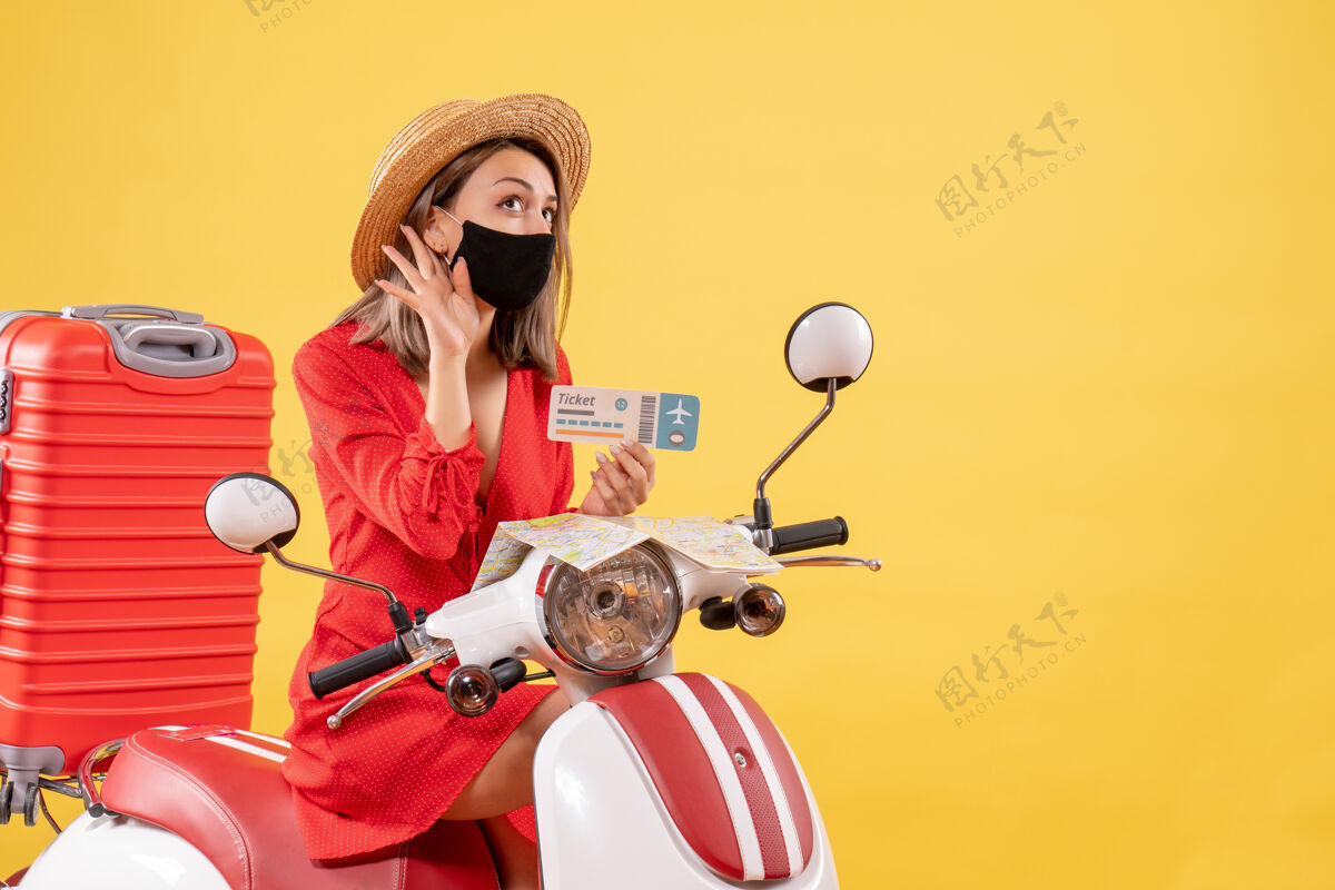 滑板车前视图：坐在轻便摩托车上的年轻女士 拿着红色手提箱 手里拿着车票 听着什么旅游人旅游