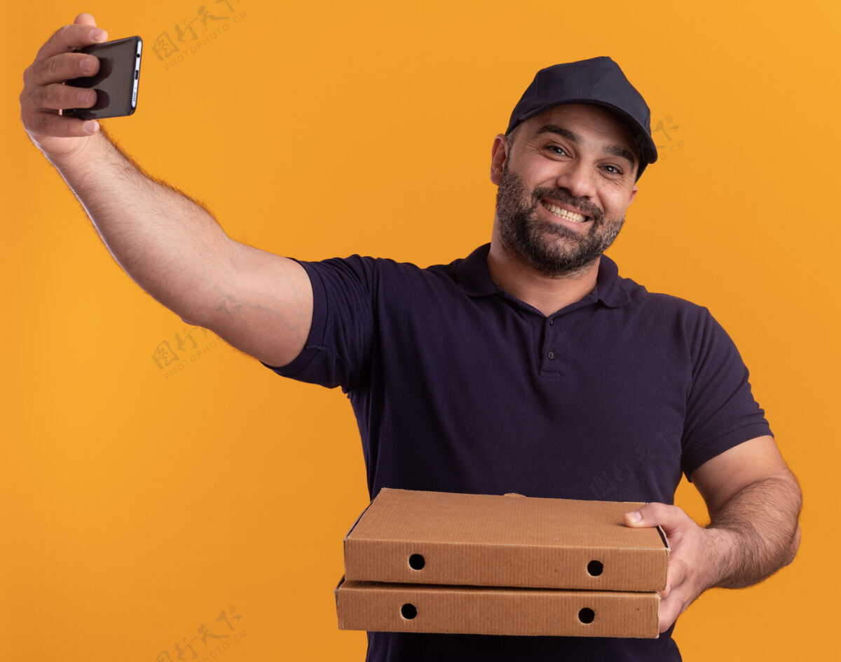 帽子微笑的中年送货员身着制服 戴着帽子 手里拿着披萨盒 独自在黄色的墙上自拍男人自拍站着
