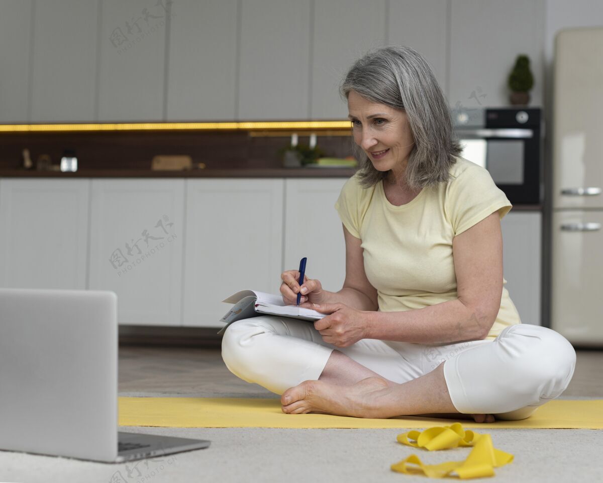 笔记本资深女士在家用笔记本电脑学习健身课并做笔记水平老年人笔记本电脑