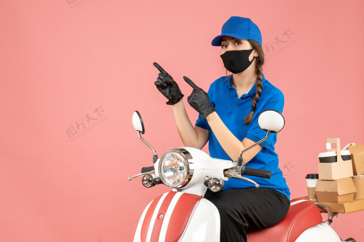 信心顶视图自信的女快递员戴着医用口罩和手套坐在滑板车上传递粉彩桃色背景下的订单命令摩托车女信使