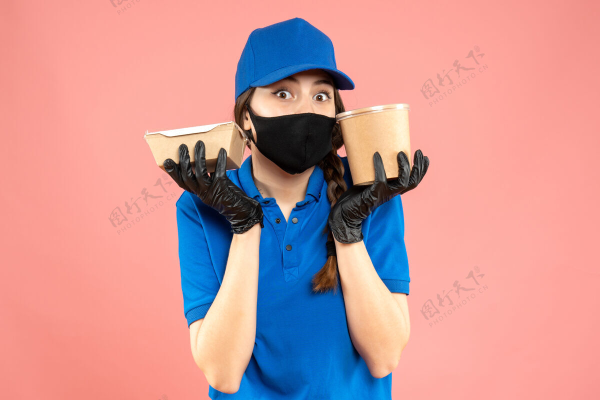 表情半身镜头惊讶的信使女孩戴着医用口罩和手套拿着粉彩桃背景上的小咖啡盒一半人身体