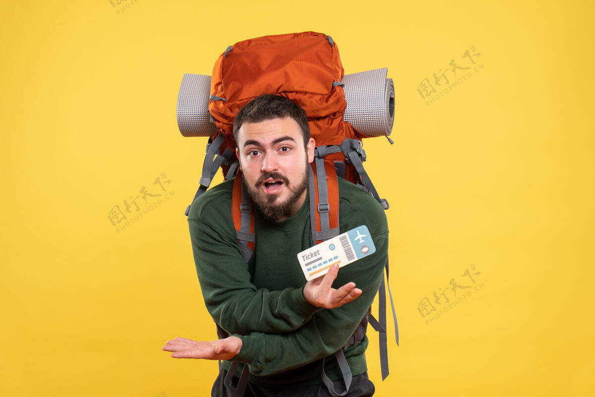 肖像年轻迷茫的旅行小伙背着背包 在黄色背景下出示车票的正面图票显示背包