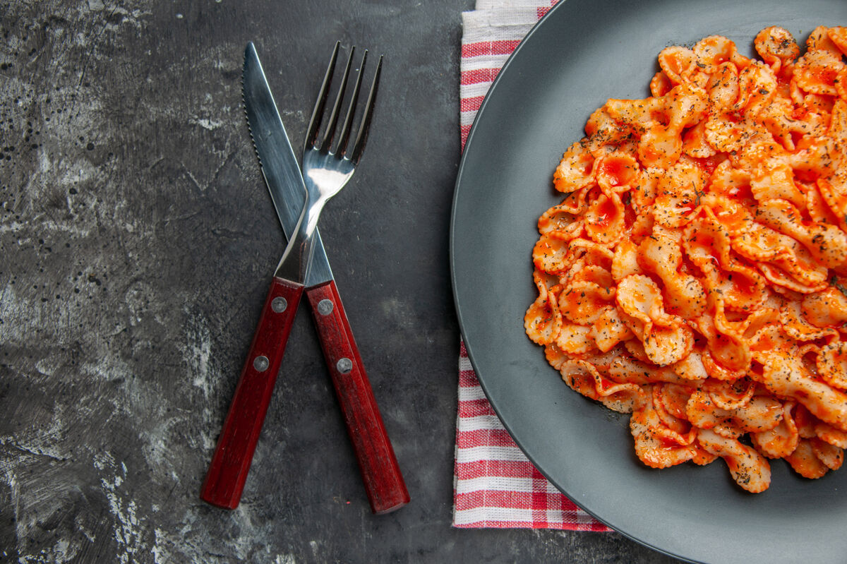 翻板机在一个黑色盘子和一套餐具上吃半杯简单的意大利面毛巾叉子食物
