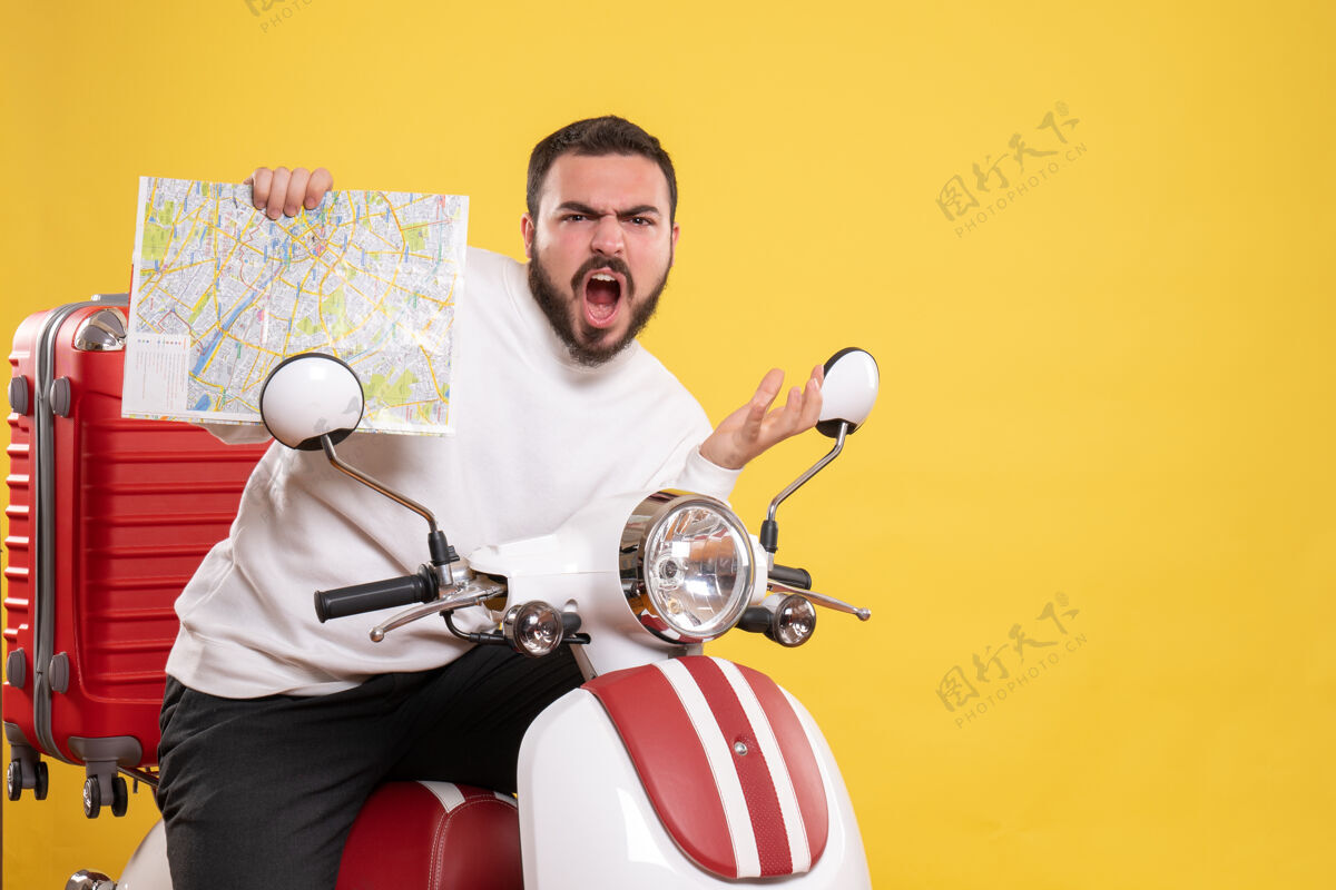 技术前视图紧张的男子坐在摩托车上 手提箱上拿着地图 背景是孤立的黄色摩托车黄色摩托车
