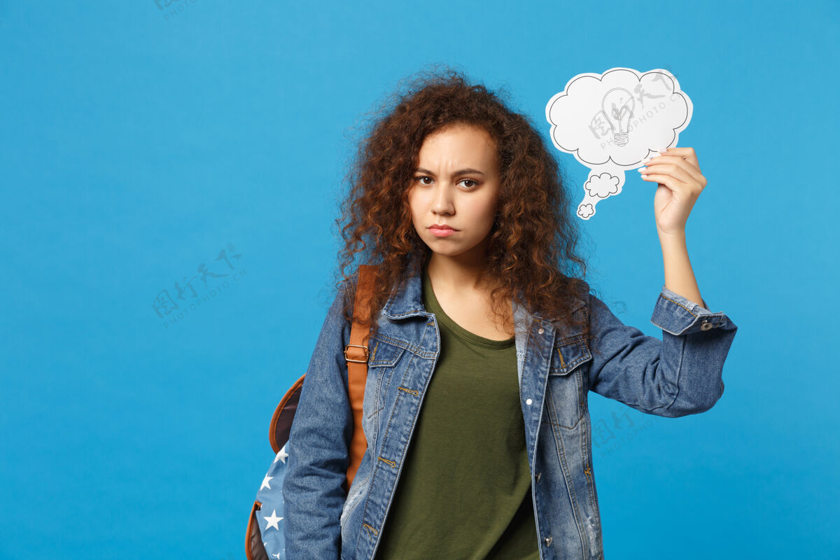 包年轻的非洲裔美国女孩十几岁的学生在牛仔服装 背包举行的蓝色墙上孤立的时钟学生立场卷发