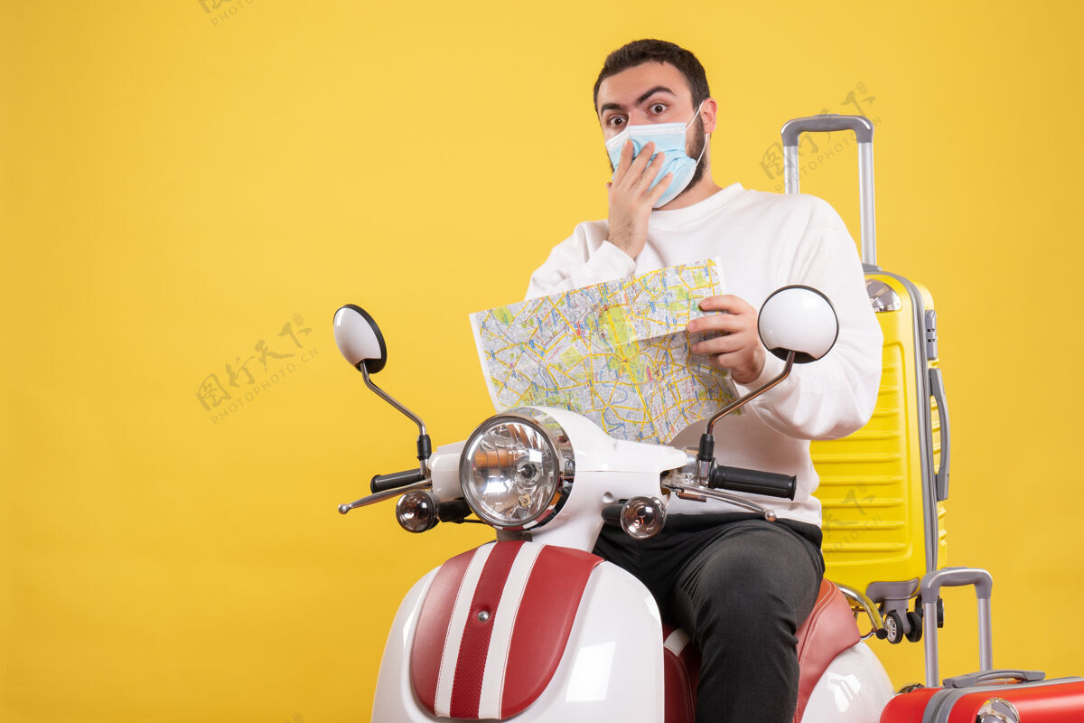 面具旅行的概念与惊讶的家伙在医疗面具坐在摩托车上 黄色的手提箱上 拿着黄色的地图摩托车黄色医疗
