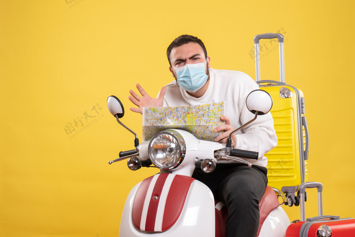 人旅行概念的俯视图 困惑的家伙戴着医用面罩坐在摩托车上 黄色手提箱放在上面 手里拿着地图安全人黄色