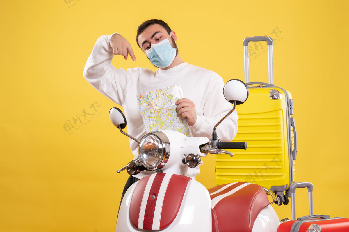 顶部旅行概念的俯视图 戴着医用面罩的自信的家伙站在摩托车旁边 黄色手提箱在上面 指着地图地图黄色运动