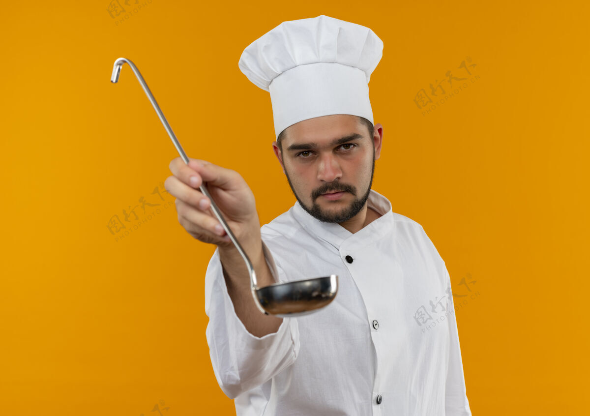 烹饪自信的年轻男厨师身着厨师制服 在橙色的墙上向孤立的人群伸出勺子年轻勺子走向