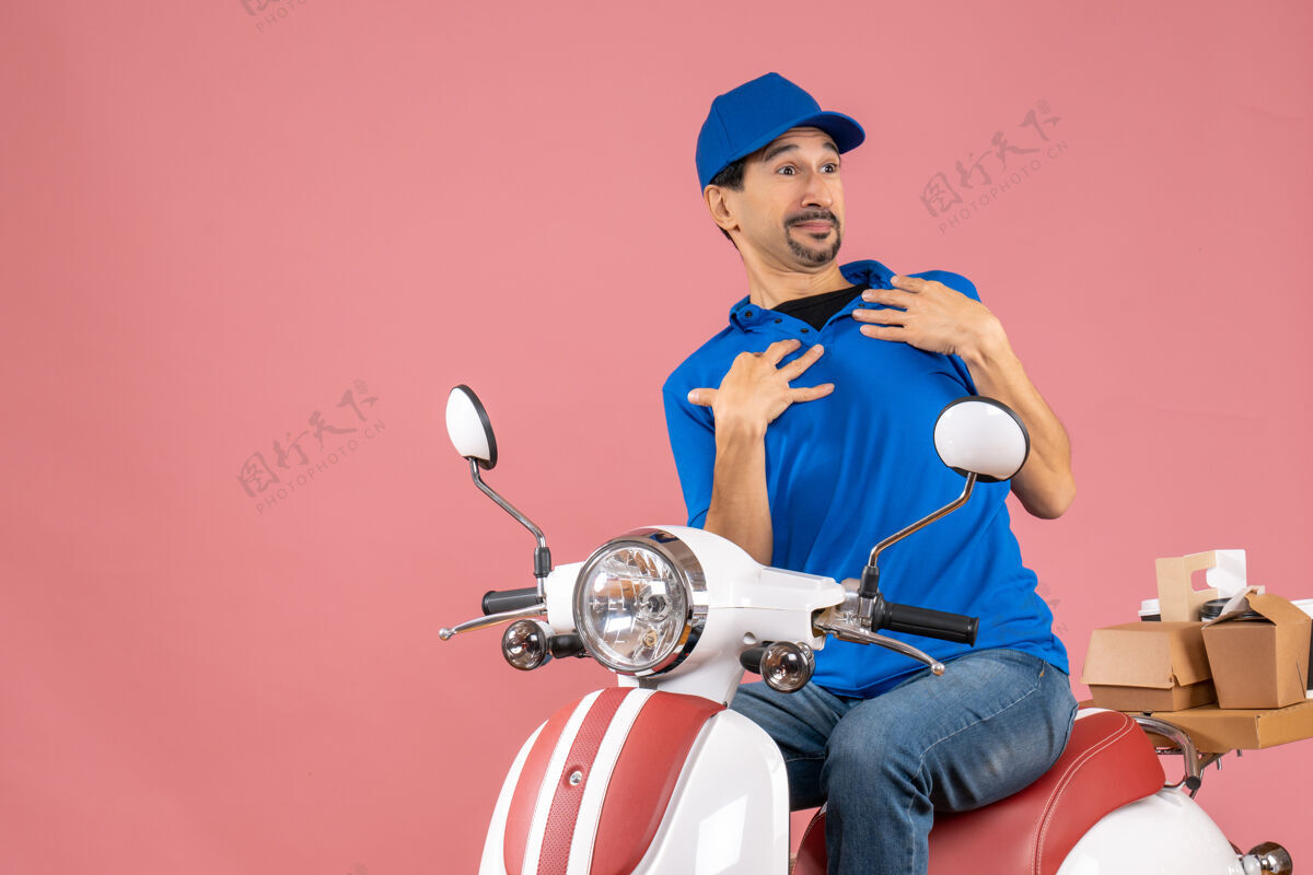 成人一个戴着帽子坐在滑板车上指着自己粉彩桃色背景的男人的前视图头盔桃子车辆