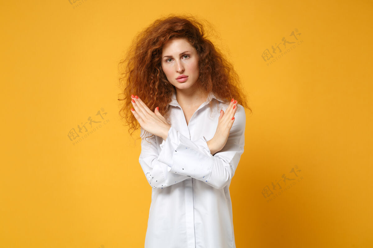 橙色穿着休闲白衬衫的年轻红发女郎在黄橙色的墙上孤零零地摆姿势手手势肖像