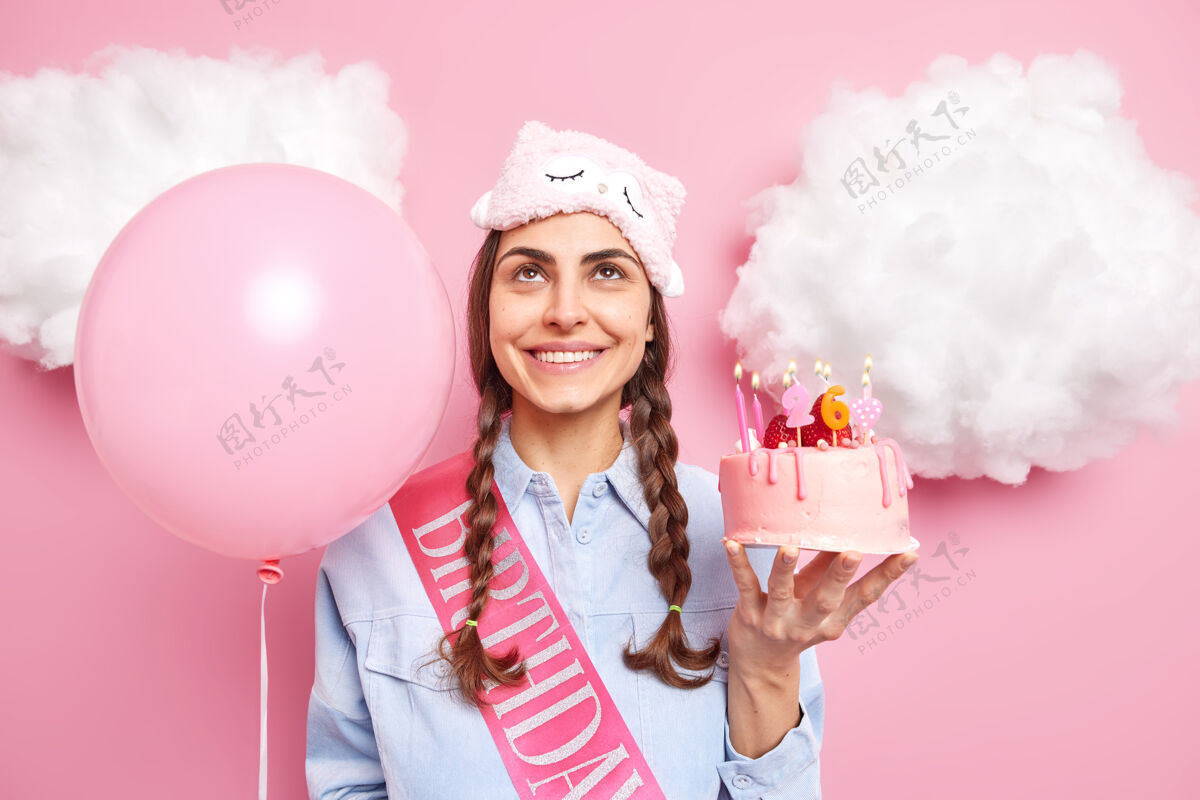 生日女人享受生日庆典手持美味的蛋糕和充气气球集中在上面随意打扮表达快乐的情绪孤立在粉红色聚会魅力睡眠面罩