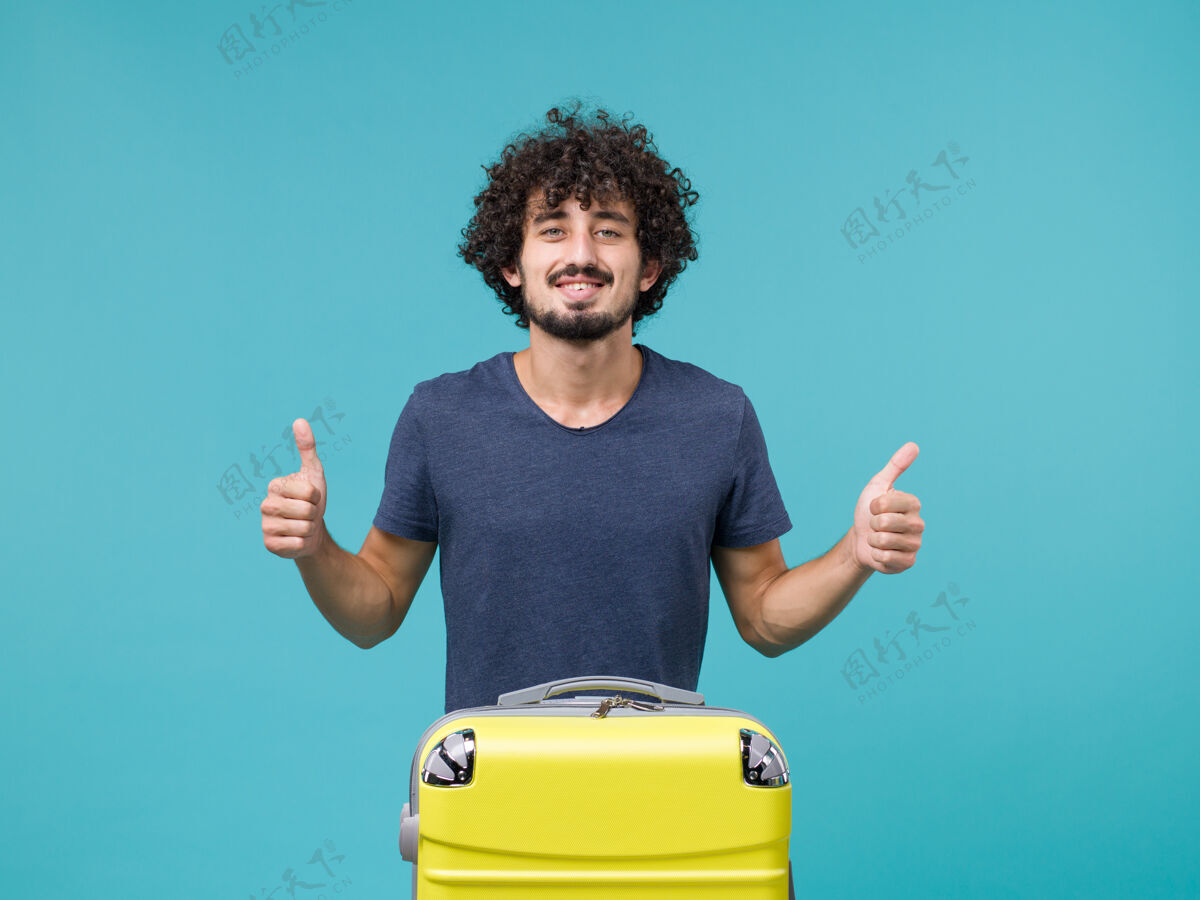 行李穿深蓝色t恤的度假男人在蓝色上微笑人工作竖起大拇指