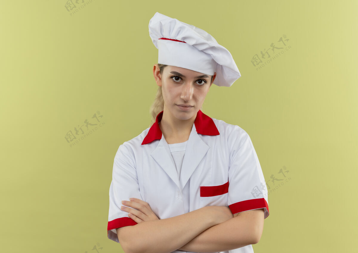 年轻自信的年轻漂亮厨师穿着厨师制服站在绿色的墙上 封闭的姿势孤立制服站立烹饪