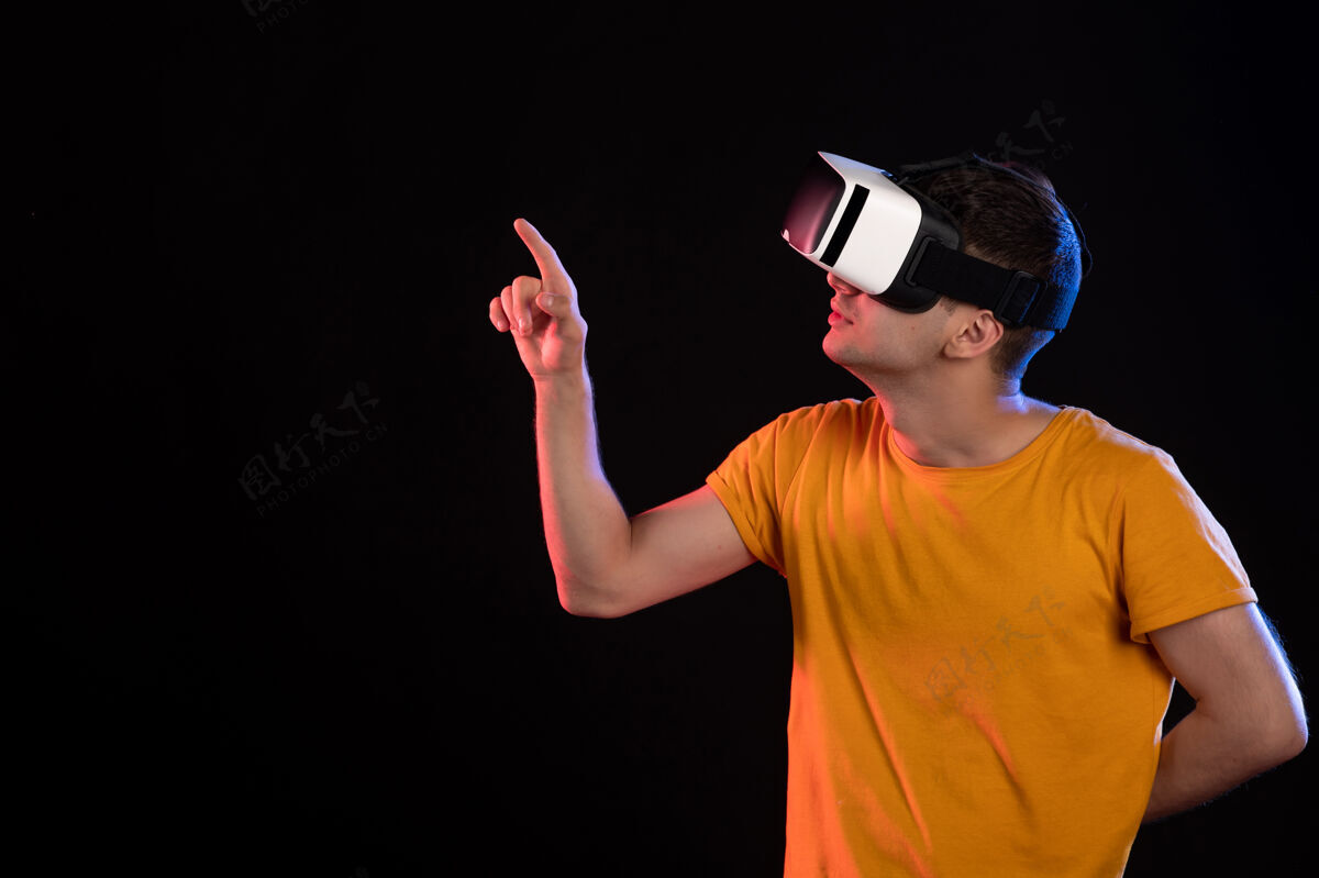 黑暗在黑暗的墙壁上玩虚拟现实的年轻男性的正面视图游戏成人男性
