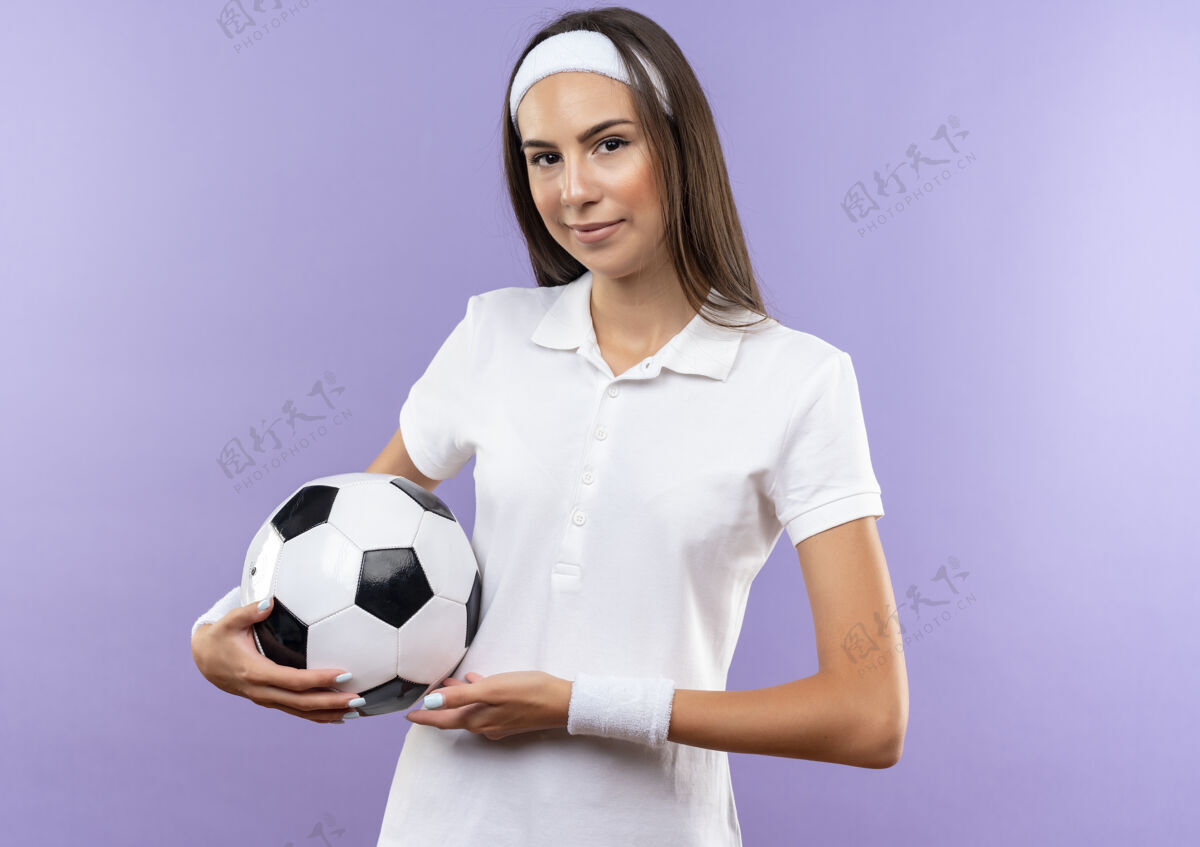 女孩自信漂亮的运动女孩戴着头带和腕带拿着足球隔离在紫色的墙上球足球自信
