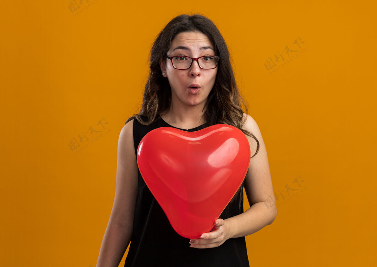年轻带着红气球的年轻美女在橙色的墙上惊喜地庆祝情人节情人节日子气球