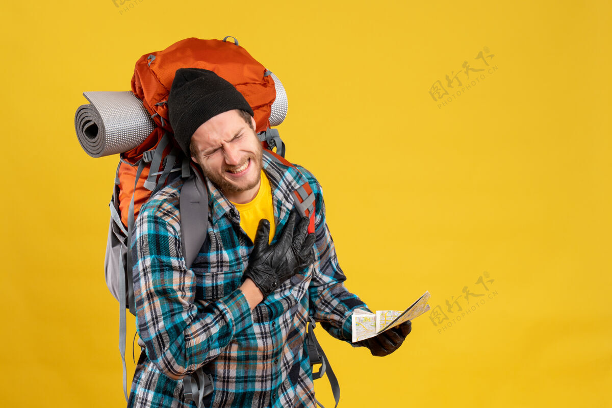 痛苦年轻的背包客带着黑色的帽子拿着旅行地图 心里带着痛苦肖像旅行男人