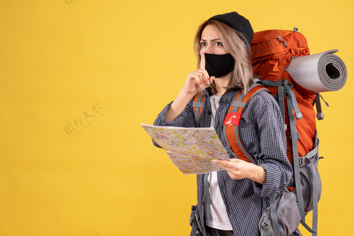 人带着黑色面具和背包的旅行女孩拿着地图做着安静的标志安静肖像面具
