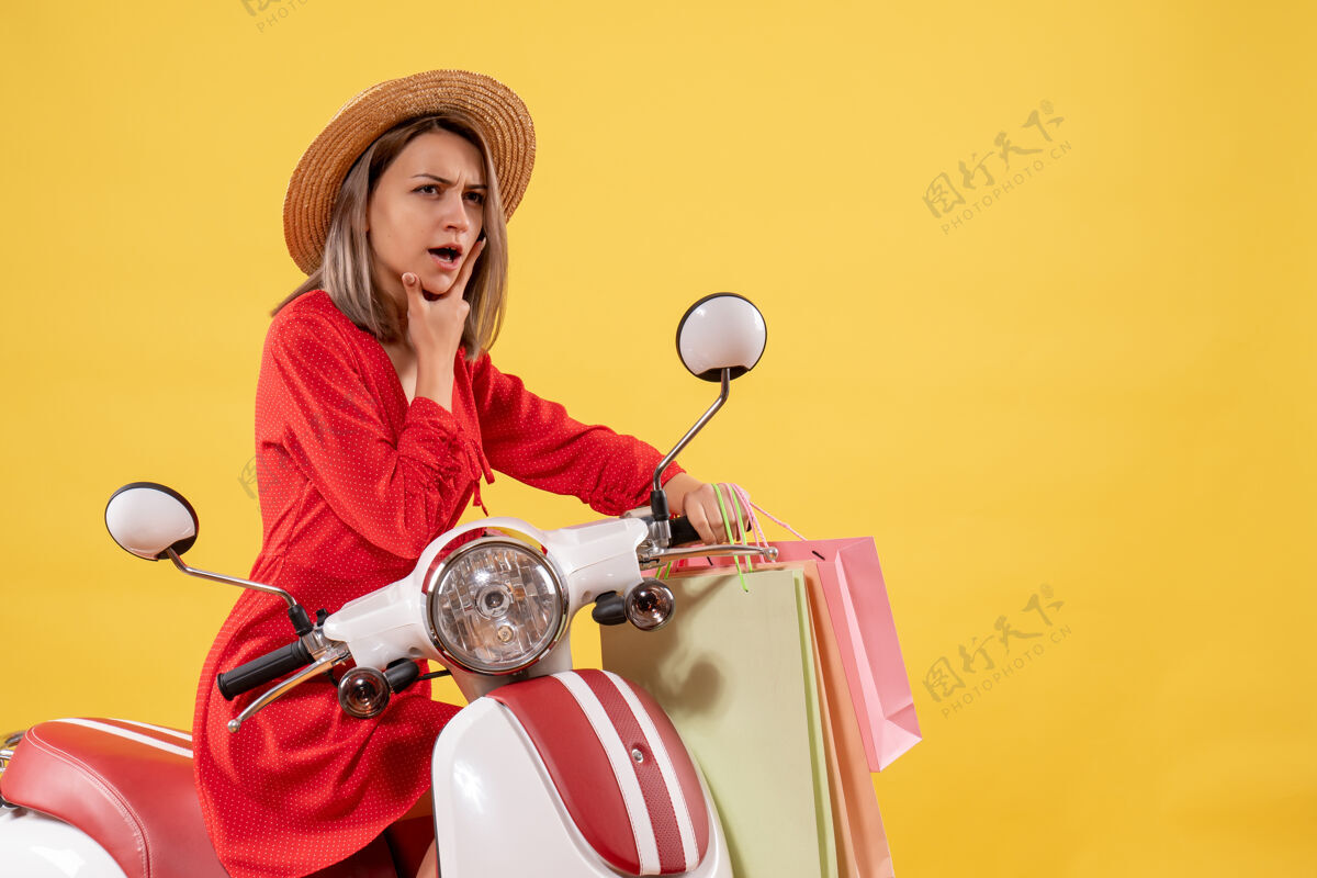 衣服体贴的女人穿着红色衣服 坐在轻便摩托车上 手里拿着购物袋人体贴的女人购物