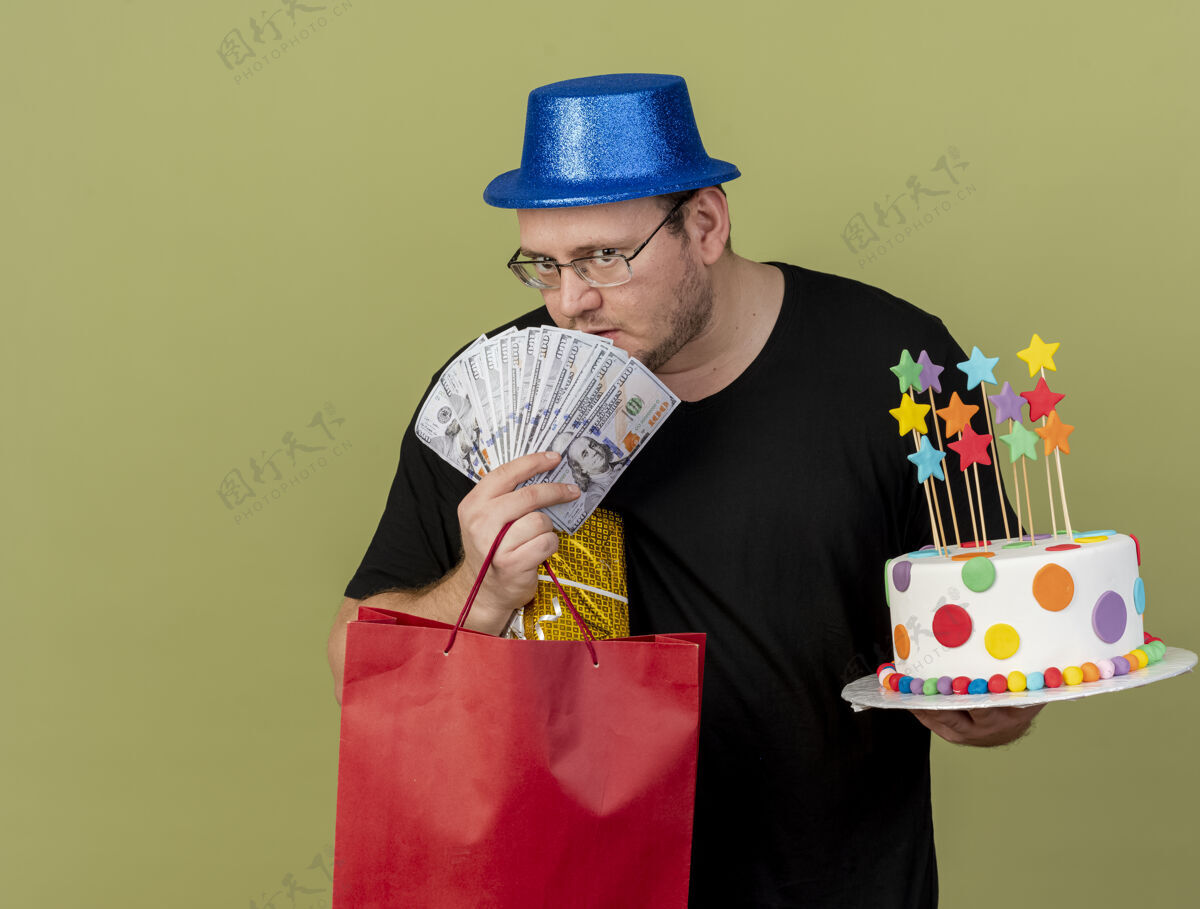 纸自信的成年斯拉夫人戴着眼镜 戴着蓝色派对帽 手里拿着钱礼盒 纸购物袋和生日蛋糕持有眼镜光学
