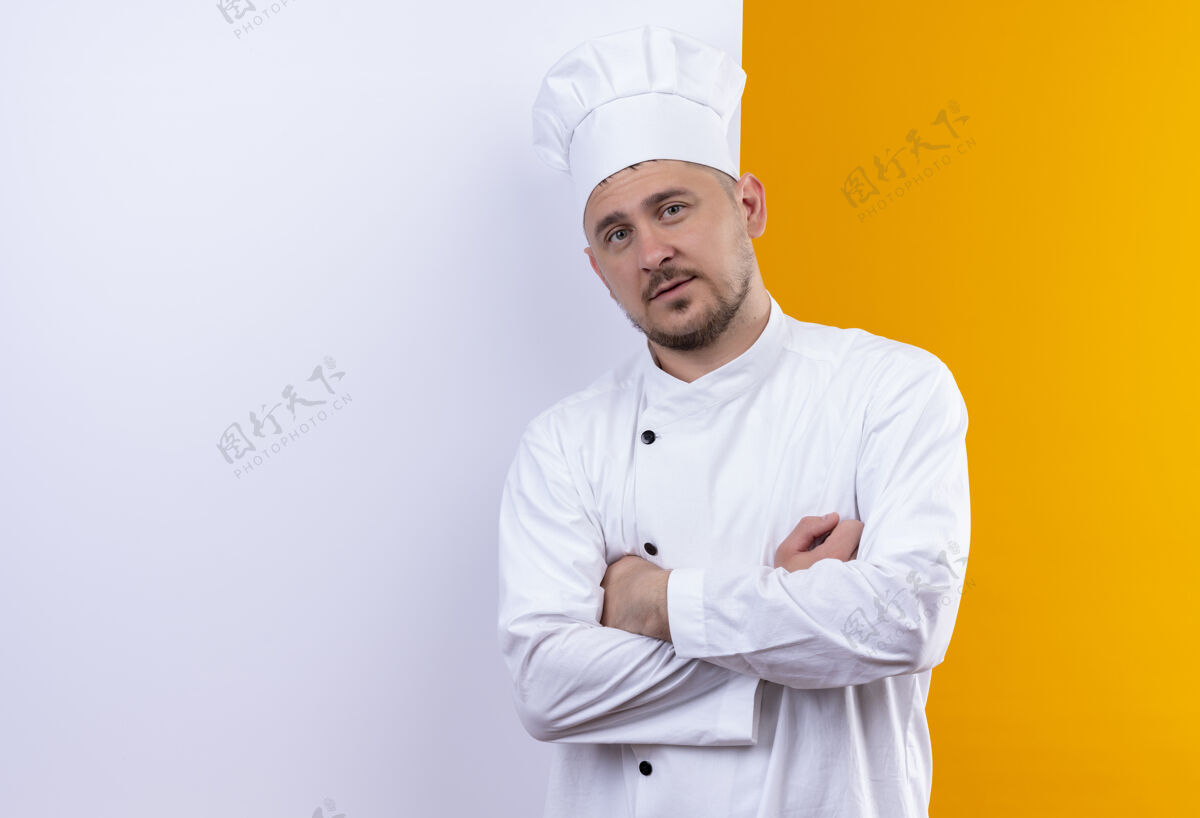 自信自信的年轻帅哥厨师身着厨师制服站在白色的墙后 橙色的墙上有一个单独的复制空间墙壁帅气年轻