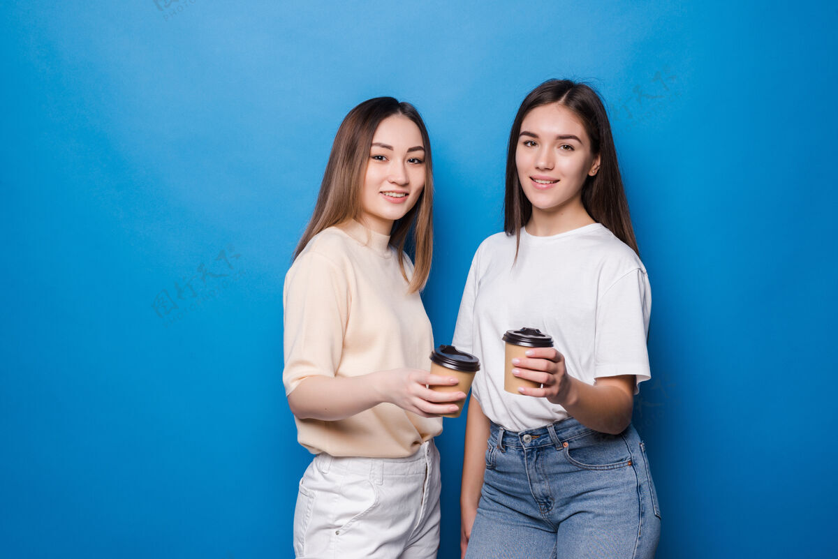 时尚两个年轻的女人拿着咖啡杯孤零零地走在蓝色的墙上咖啡太阳镜非洲
