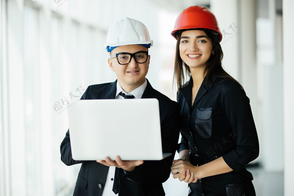微笑工程和建筑概念工程师拿着笔记本电脑在建筑工地上工作 男建筑师和女工程师在工作场所检查建筑平面图公司讨论工人