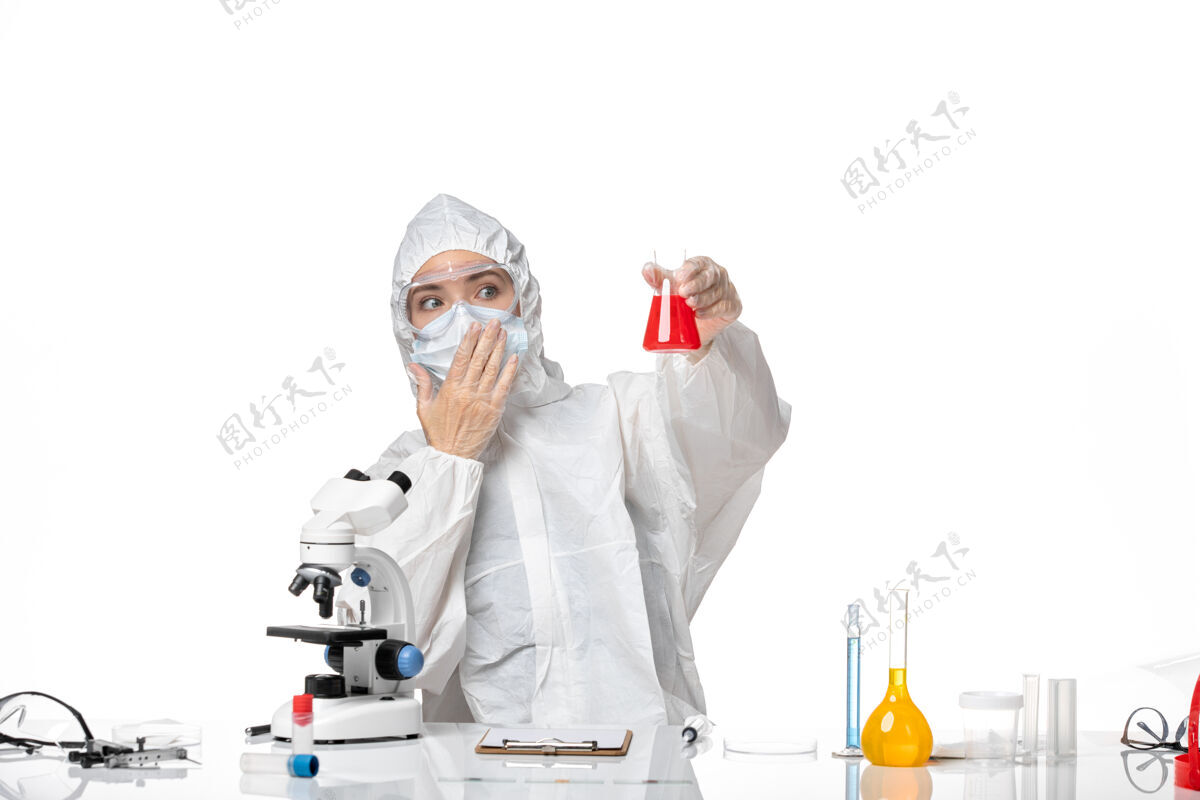 病毒正面图年轻女医生穿着白色防护服 戴着口罩 由于柯维德手持红色溶液 白色背景病毒大流行飞溅柯维德-面罩套装溶液