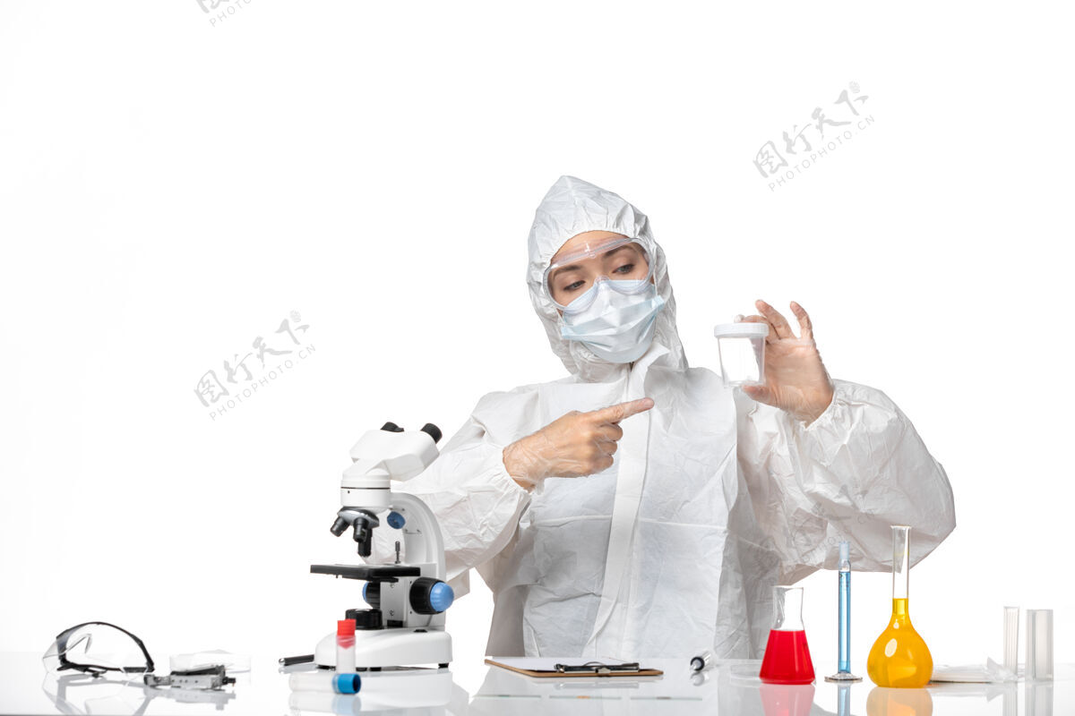 专业正面图年轻女医生穿着防护服 戴着口罩 因为白色背景上有一个装着柯维德病毒的瓶子套装药品口罩