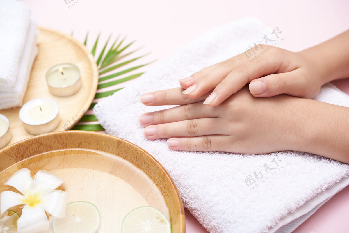 湿女士用碗里的水和鲜花浸泡双手 为女士提供足部和手部spa治疗和产品 按摩鹅卵石 香水 水和蜡烛 放松平躺俯视图健康碗人