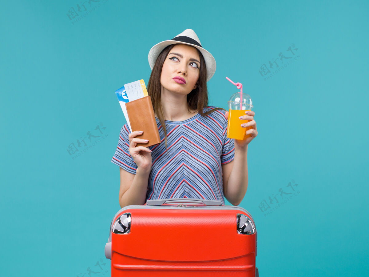 旅行正面图：度假中的女人拿着新鲜的果汁和蓝色背景的机票去度假海上避暑票旅行果汁