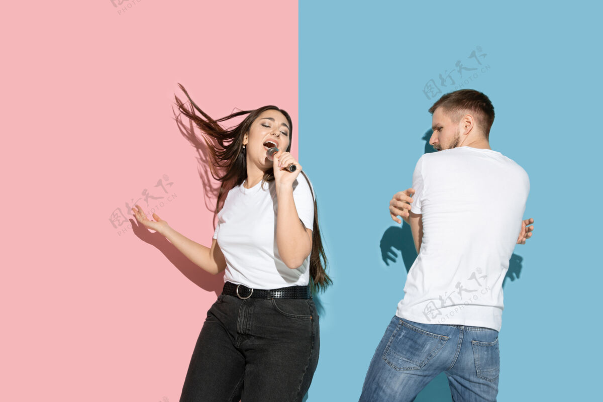 时尚年轻快乐的男女穿着休闲装在粉色 蓝色的双色墙上 载歌载舞女人人类情侣