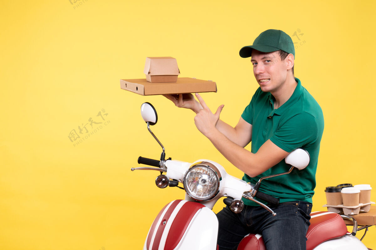 摩托车正面图身着制服的年轻男性快递员手持黄色食品包装运输机货箱工作