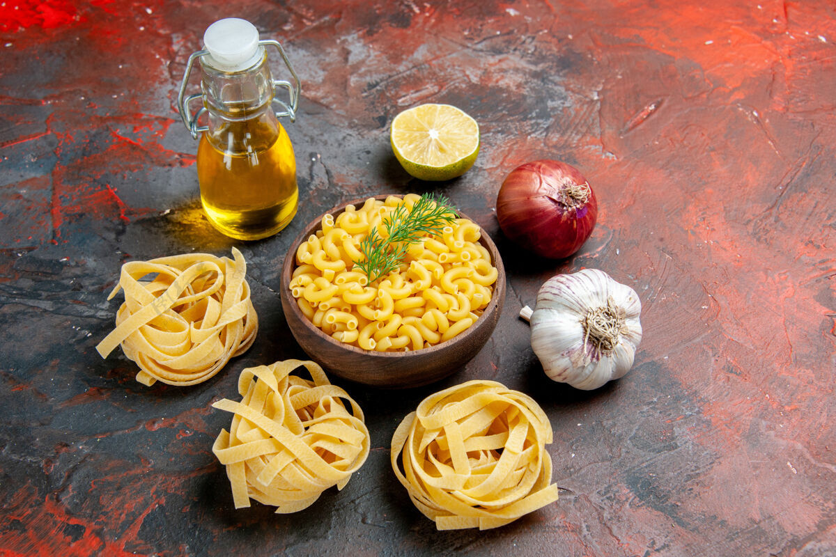 午餐三个生的意大利面和蝴蝶面放在一个棕色的碗里 葱柠檬蒜油瓶放在混合色的背景上饭菜食物柠檬