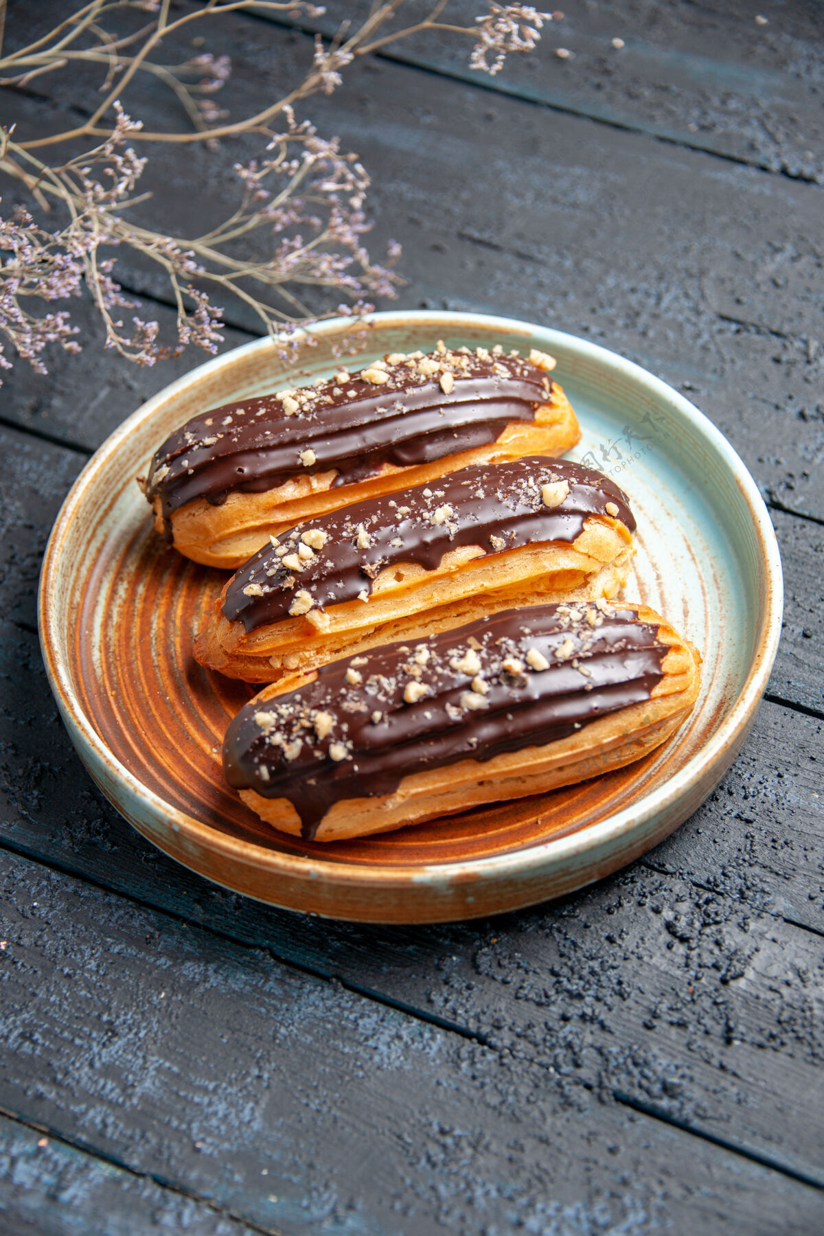 盘子底视图巧克力eclairs椭圆形板上干花枝上的黑色木制背景底部饼干一餐