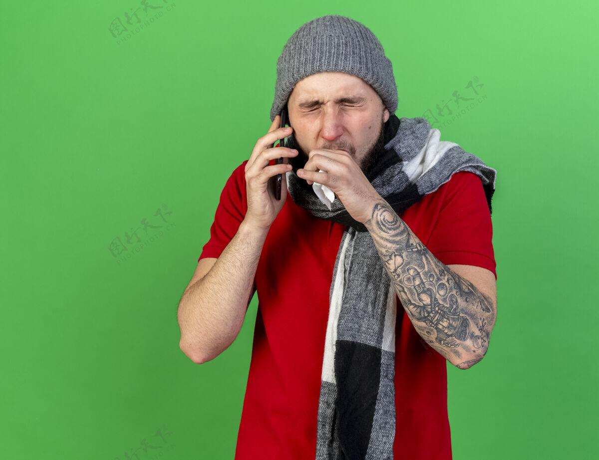 男人咳嗽的年轻白人病人戴着冬天的帽子和围巾拿着纸巾打电话电话围巾冬天