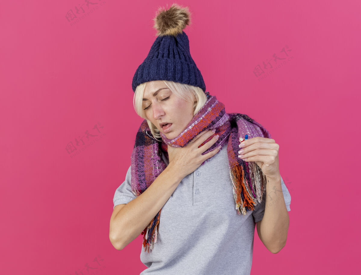 药片一个年轻的金发病斯拉夫女人戴着冬天的帽子和围巾 手放在脖子上斯拉夫脖子医疗